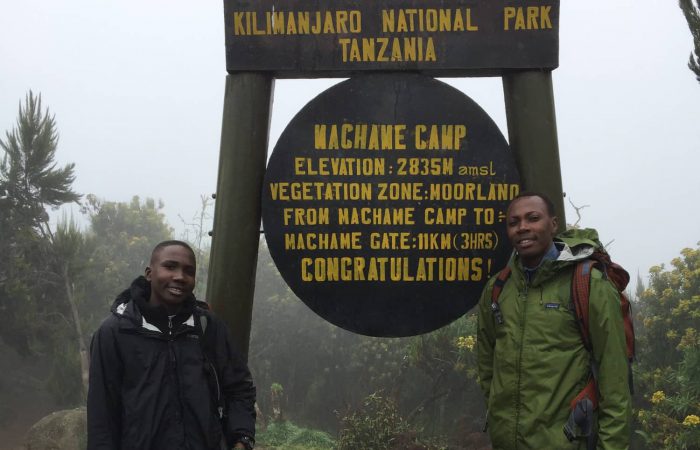 Trekkers at the Machame Camp welcome sign on the Kilimanjaro Machame route day trek